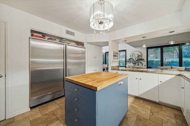 kitchen featuring built in fridge, stone tile floors, butcher block counters, blue cabinets, and white cabinetry
