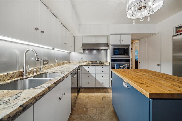 kitchen featuring a sink, stone tile floors, butcher block counters, stainless steel appliances, and white cabinetry
