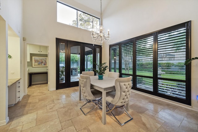 dining room with stone tile flooring, a chandelier, plenty of natural light, baseboards, and a towering ceiling
