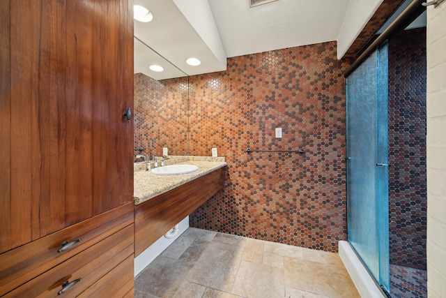bathroom featuring a stall shower, stone tile floors, vanity, and tile walls