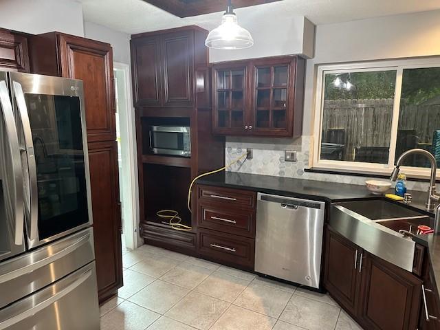 kitchen featuring appliances with stainless steel finishes, a sink, light tile patterned floors, and dark countertops