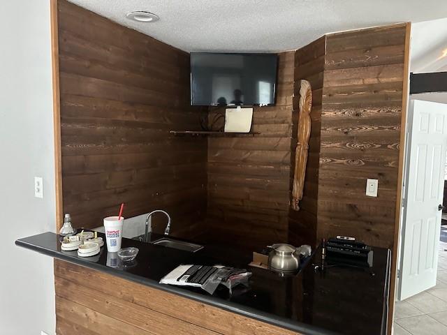 bar featuring wood walls, a sink, tile patterned floors, and a textured ceiling