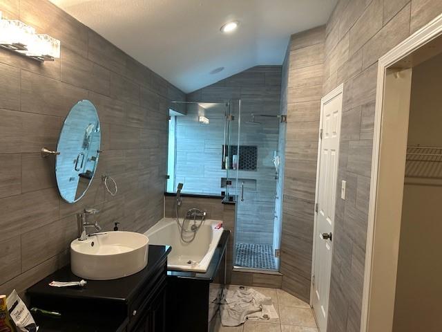 bathroom with tile walls, vaulted ceiling, a shower stall, a bath, and tile patterned floors