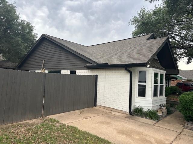 view of home's exterior with roof with shingles, fence, and brick siding