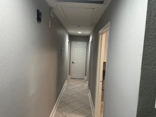 corridor featuring light tile patterned flooring, attic access, and baseboards