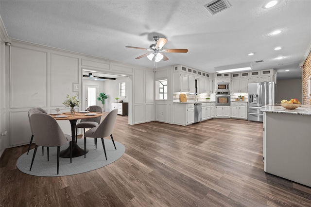 6211 Sjolander Rd, Baytown, TX 77521 - kitchen with stainless steel appliances, a ceiling fan, a decorative wall, dark wood-style floors, and white cabinets