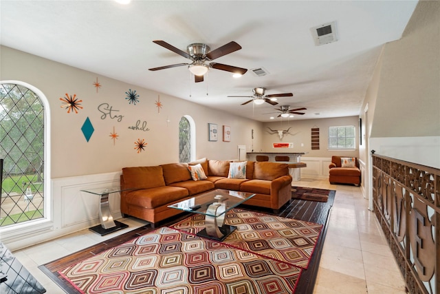 living room featuring a ceiling fan, wainscoting, a decorative wall, and light tile patterned floors
