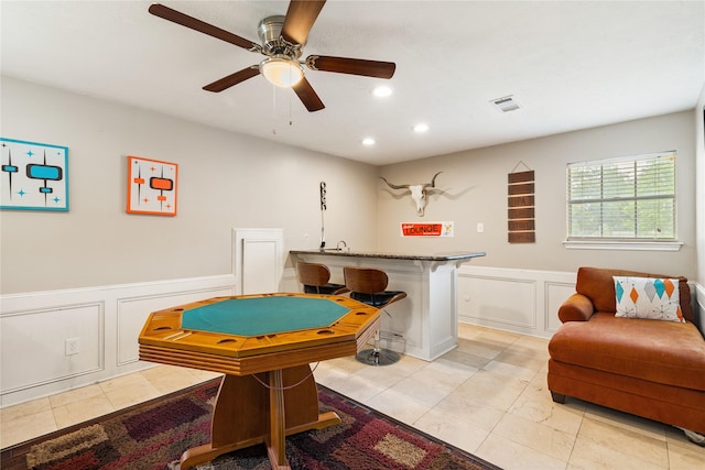 recreation room with a decorative wall, light tile patterned floors, recessed lighting, a ceiling fan, and wainscoting