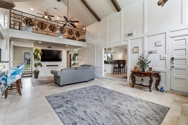 living area with a high ceiling, a decorative wall, plenty of natural light, a ceiling fan, and light tile patterned floors