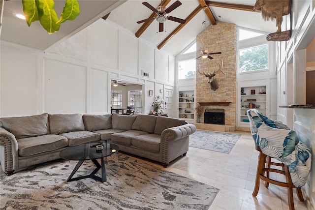living area featuring ceiling fan, a decorative wall, high vaulted ceiling, built in shelves, and a stone fireplace