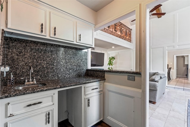kitchen with a sink, a decorative wall, decorative backsplash, dark stone counters, and white cabinets