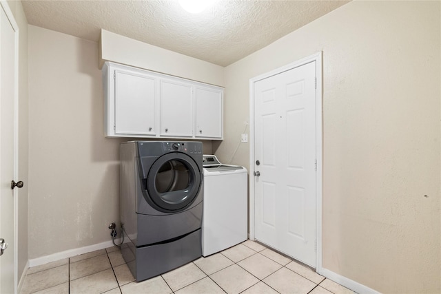 clothes washing area featuring separate washer and dryer, cabinet space, light tile patterned floors, baseboards, and a textured ceiling