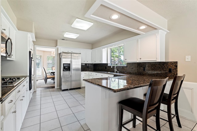 kitchen featuring appliances with stainless steel finishes, a peninsula, a sink, dark stone counters, and white cabinets