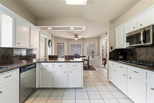 kitchen with appliances with stainless steel finishes, a peninsula, light tile patterned floors, white cabinets, and ceiling fan