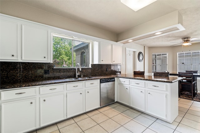 kitchen featuring stainless steel dishwasher, a sink, a peninsula, white cabinetry, and decorative backsplash