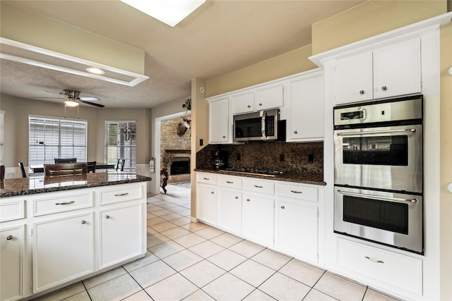 kitchen with stainless steel appliances, a fireplace, white cabinetry, light tile patterned floors, and tasteful backsplash