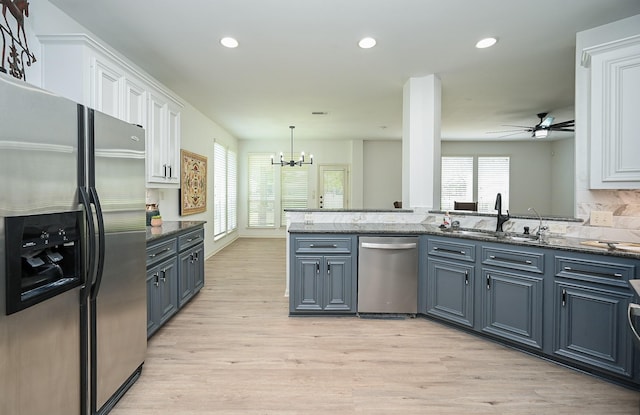 kitchen with appliances with stainless steel finishes, white cabinetry, a sink, light wood-style flooring, and a chandelier