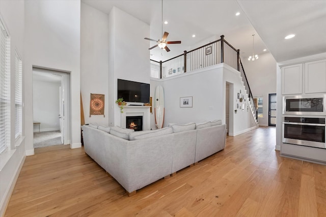 10059 Preserve Way, Conroe, TX 77385 - living room with a towering ceiling, a glass covered fireplace, a ceiling fan, light wood-type flooring, and baseboards