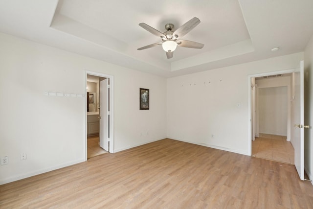 unfurnished bedroom featuring a raised ceiling, light wood-type flooring, baseboards, and a ceiling fan