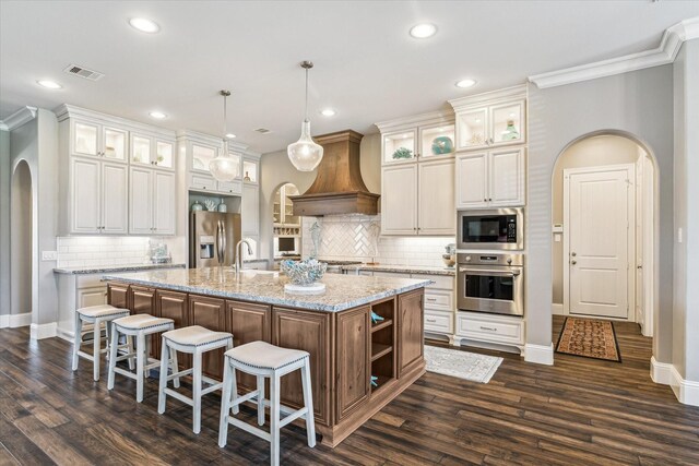 32319 Tall Oaks Way, Magnolia, TX 77354 - kitchen with stainless steel appliances, arched walkways, premium range hood, baseboards, and ornamental molding