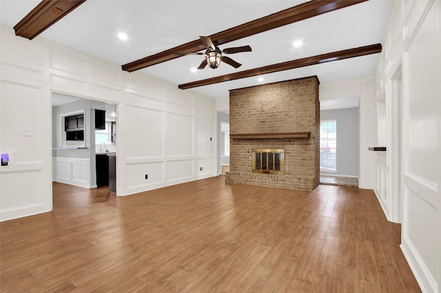 6214 Oak Masters Dr, Spring, TX 77379 - unfurnished living room featuring a decorative wall, ceiling fan, beamed ceiling, light wood-style flooring, and a brick fireplace