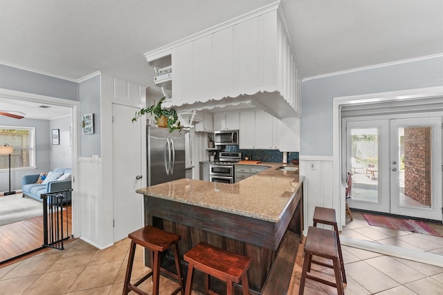 10438 Brinwood Dr, Houston, TX 77043 - kitchen with stainless steel appliances, light tile patterned floors, light stone countertops, crown molding, and white cabinetry