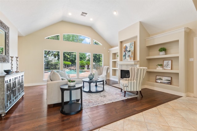 living area with built in features, a tiled fireplace, hardwood / wood-style flooring, vaulted ceiling, and recessed lighting