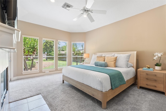 carpeted bedroom with a glass covered fireplace, tile patterned flooring, and ceiling fan