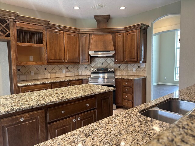 305 Tyler Dr, Bridge City, TX 77630 - kitchen featuring stainless steel electric range, arched walkways, under cabinet range hood, backsplash, and light stone countertops