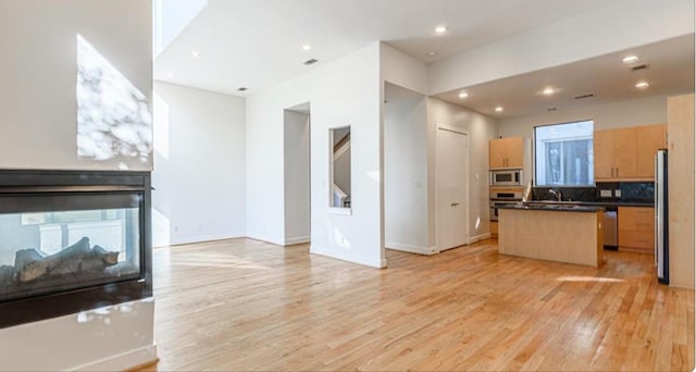 730 Ruthven, Houston, TX 77019 - kitchen featuring open floor plan, a center island with sink, appliances with stainless steel finishes, dark countertops, and light wood-type flooring