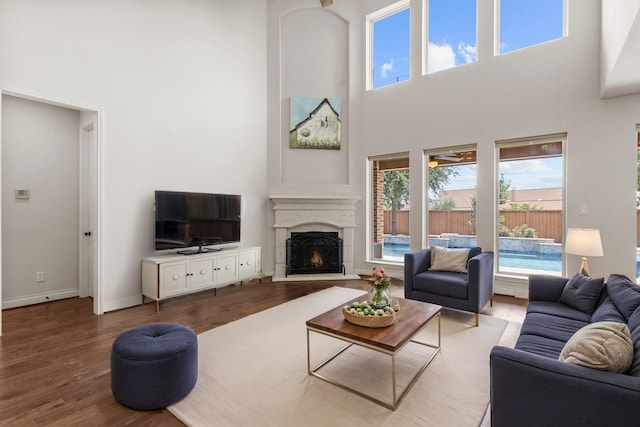 living area featuring a high ceiling, wood finished floors, a lit fireplace, and baseboards