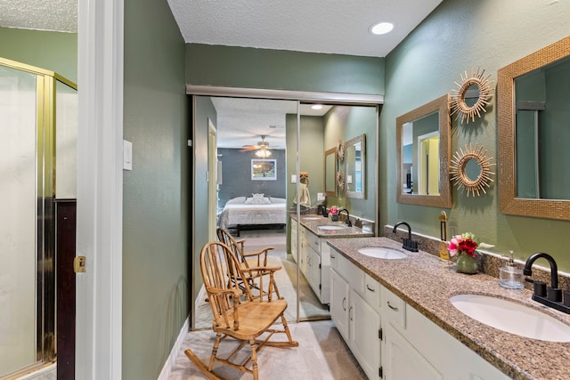 ensuite bathroom featuring a textured ceiling, a stall shower, a ceiling fan, a textured wall, and double vanity