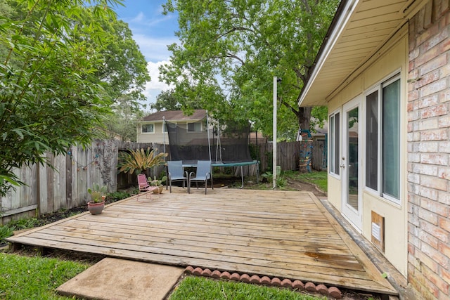wooden terrace with a trampoline and a fenced backyard