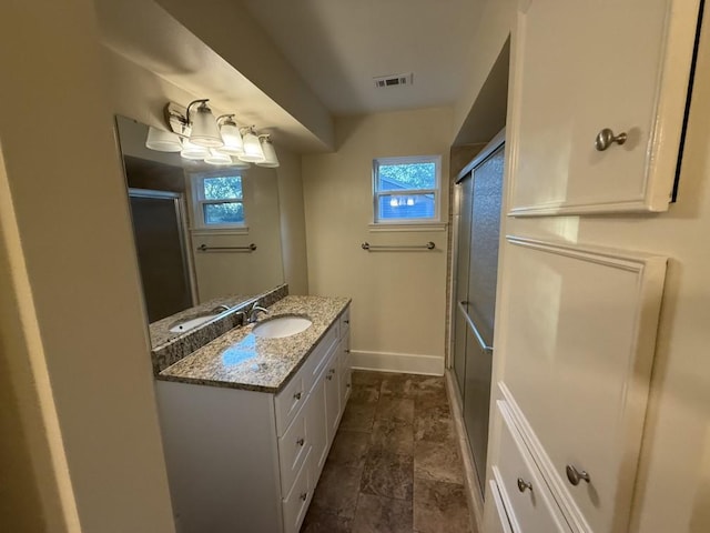 bathroom with baseboards, healthy amount of natural light, vanity, and stone finish floors