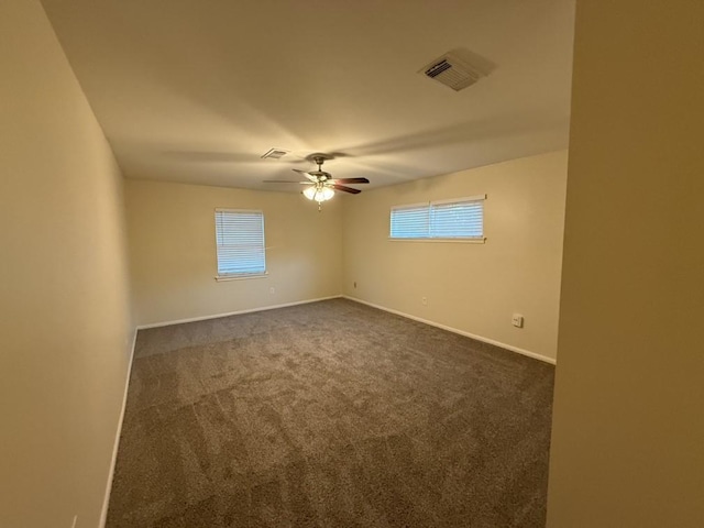 unfurnished room with plenty of natural light, dark carpet, ceiling fan, and baseboards