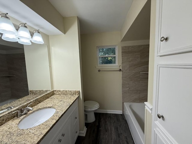 bathroom with wood finished floors, vanity, toilet, baseboards, and a bathtub
