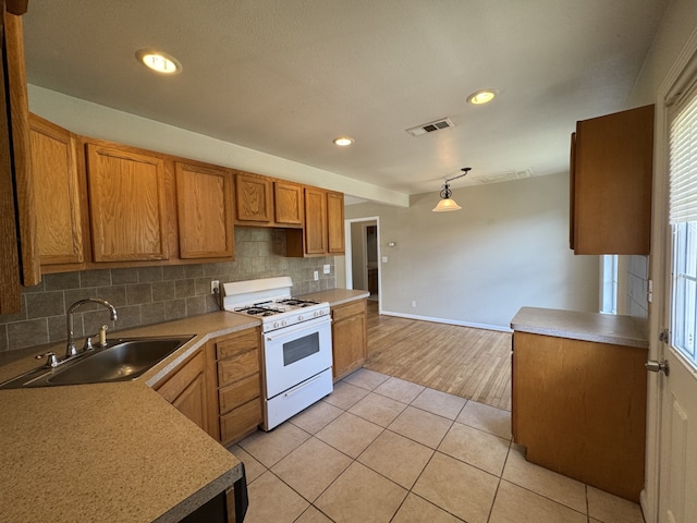 216 Gale St, Houston, TX 77009 - kitchen featuring white gas range oven, a sink, decorative backsplash, brown cabinets, and light tile patterned flooring