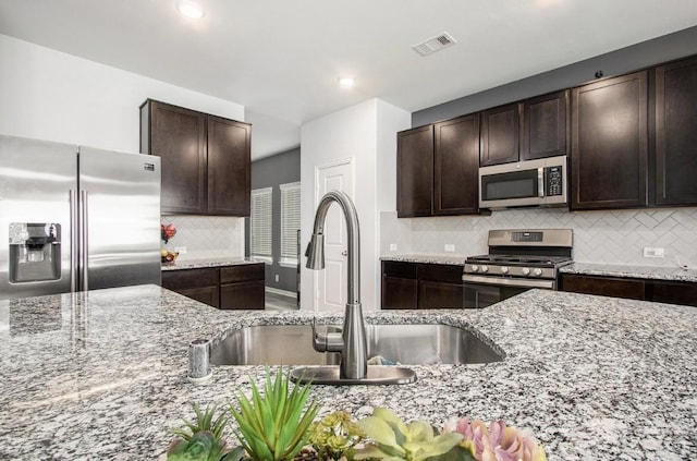10906 Granite Chief Dr, Rosharon, TX 77583 - kitchen featuring stainless steel appliances, a sink, decorative backsplash, light stone countertops, and dark brown cabinetry