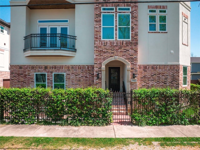 view of front of property featuring a balcony, brick siding, fence, and stucco siding