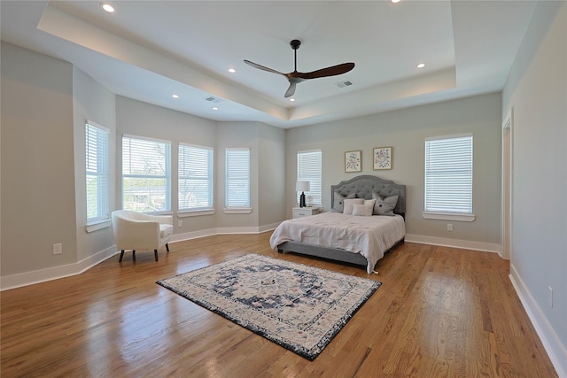 bedroom featuring a raised ceiling, wood finished floors, baseboards, recessed lighting, and a ceiling fan