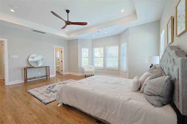 bedroom with a tray ceiling, wood finished floors, recessed lighting, baseboards, and ceiling fan