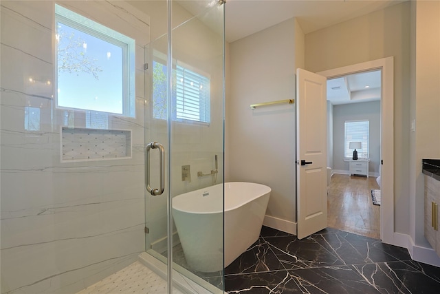 bathroom with marble tiled floors, healthy amount of natural light, a shower stall, and a soaking tub