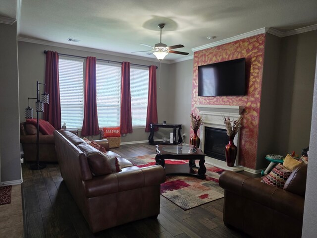 living area with dark wood finished floors, a ceiling fan, a fireplace with raised hearth, crown molding, and baseboards