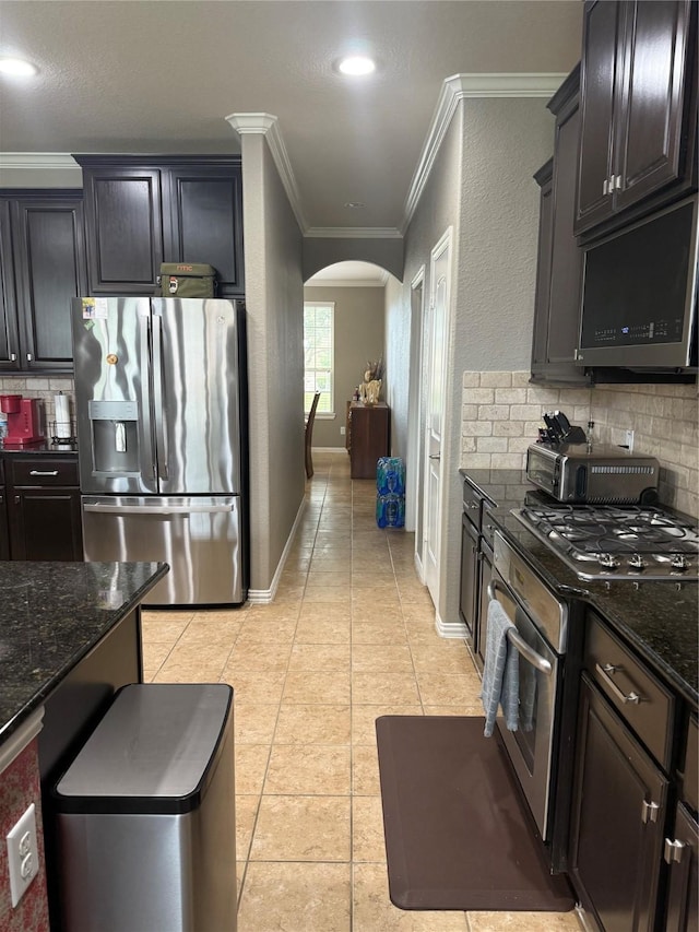 kitchen with appliances with stainless steel finishes, arched walkways, crown molding, tasteful backsplash, and light tile patterned flooring