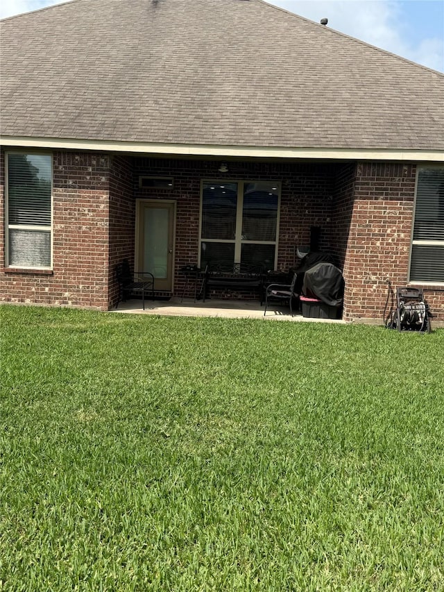 back of house with a patio area, a shingled roof, a lawn, and brick siding