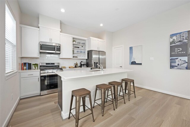 1013 Erin St Unit A, Houston, TX 77009 - kitchen featuring stainless steel appliances, open shelves, light wood-style floors, a center island with sink, and recessed lighting