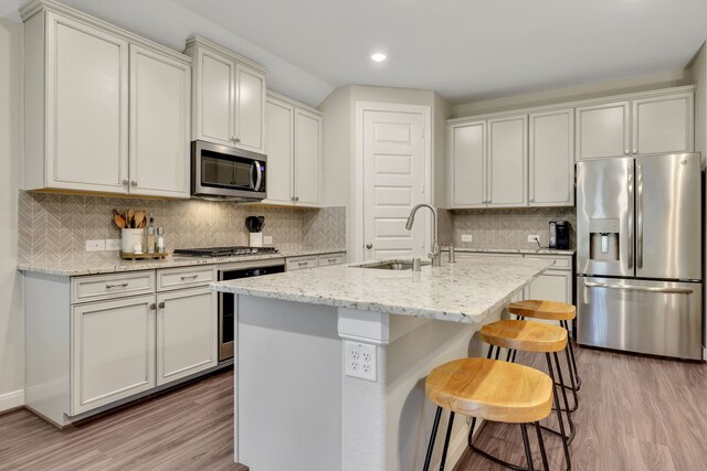 21310 Baldovin Way, Tomball, TX 77375 - kitchen featuring stainless steel appliances, a sink, light wood-type flooring, a kitchen bar, and decorative backsplash