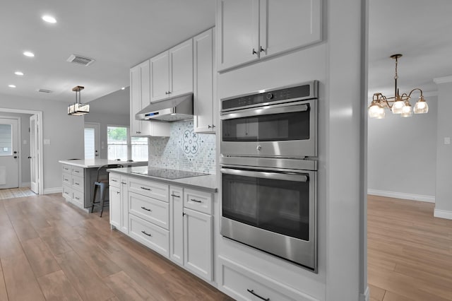 2806 Triway Ln, Houston, TX 77043 - kitchen with stainless steel double oven, under cabinet range hood, black electric cooktop, light wood-type flooring, and recessed lighting