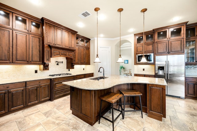 kitchen featuring a sink, appliances with stainless steel finishes, tasteful backsplash, crown molding, and a center island with sink