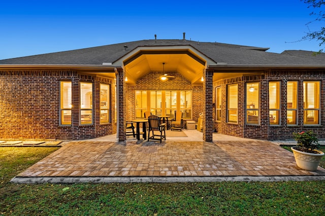 back of property featuring brick siding, a patio, and roof with shingles